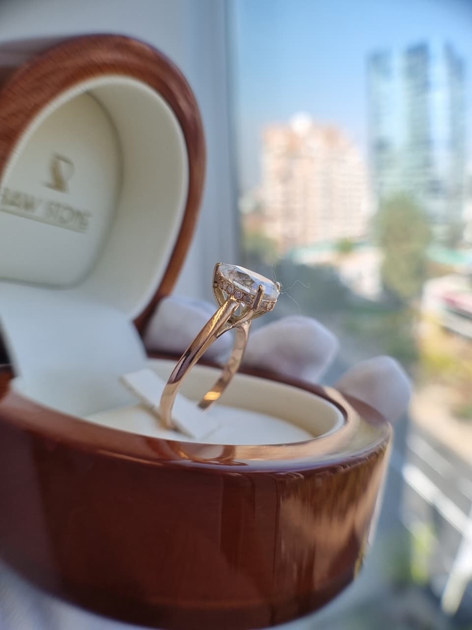 Anillo de compromiso con diamante esmeralda entre dos dedos con bokeh dorado